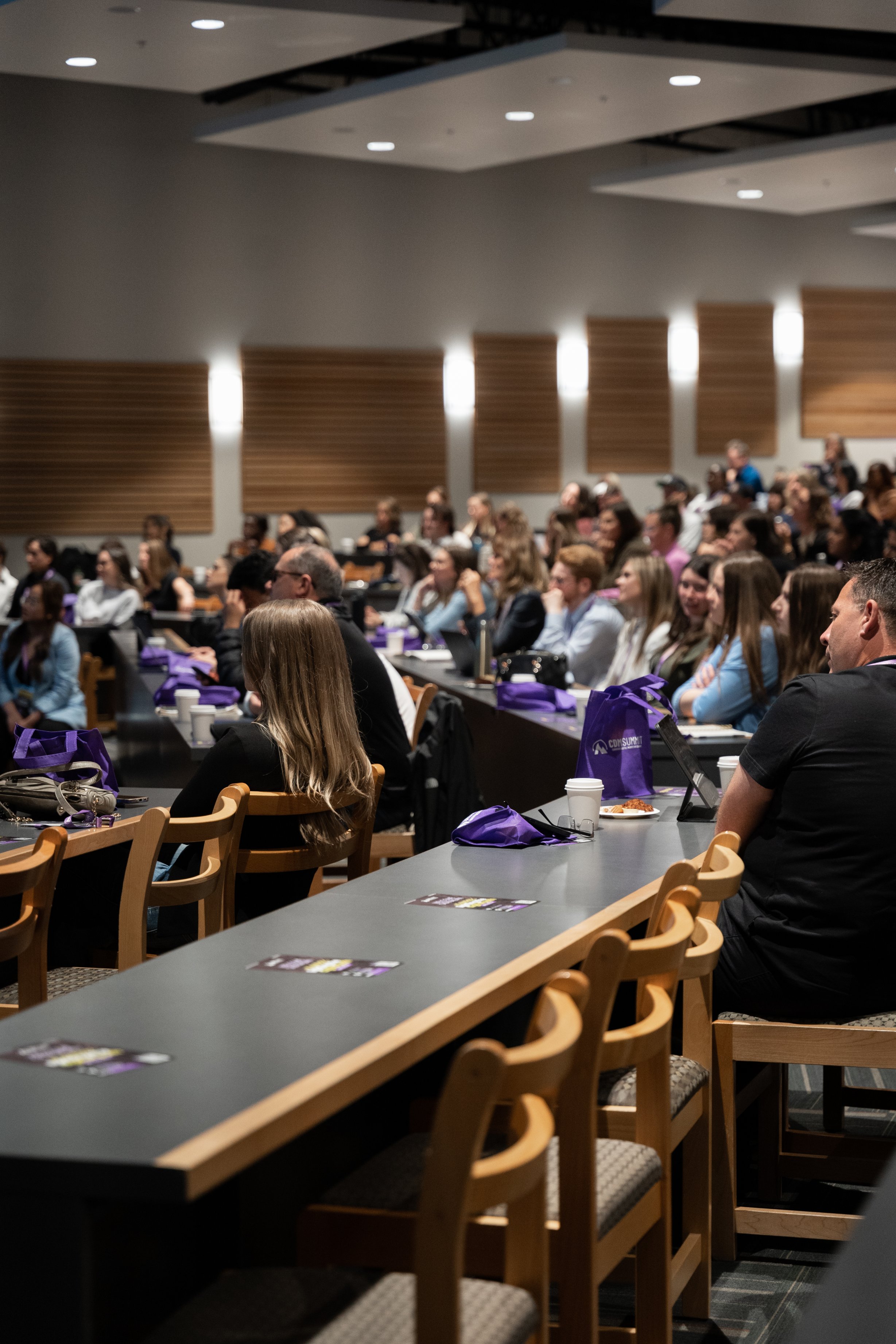 CDM Summit audience seated at tables with purple summit bags