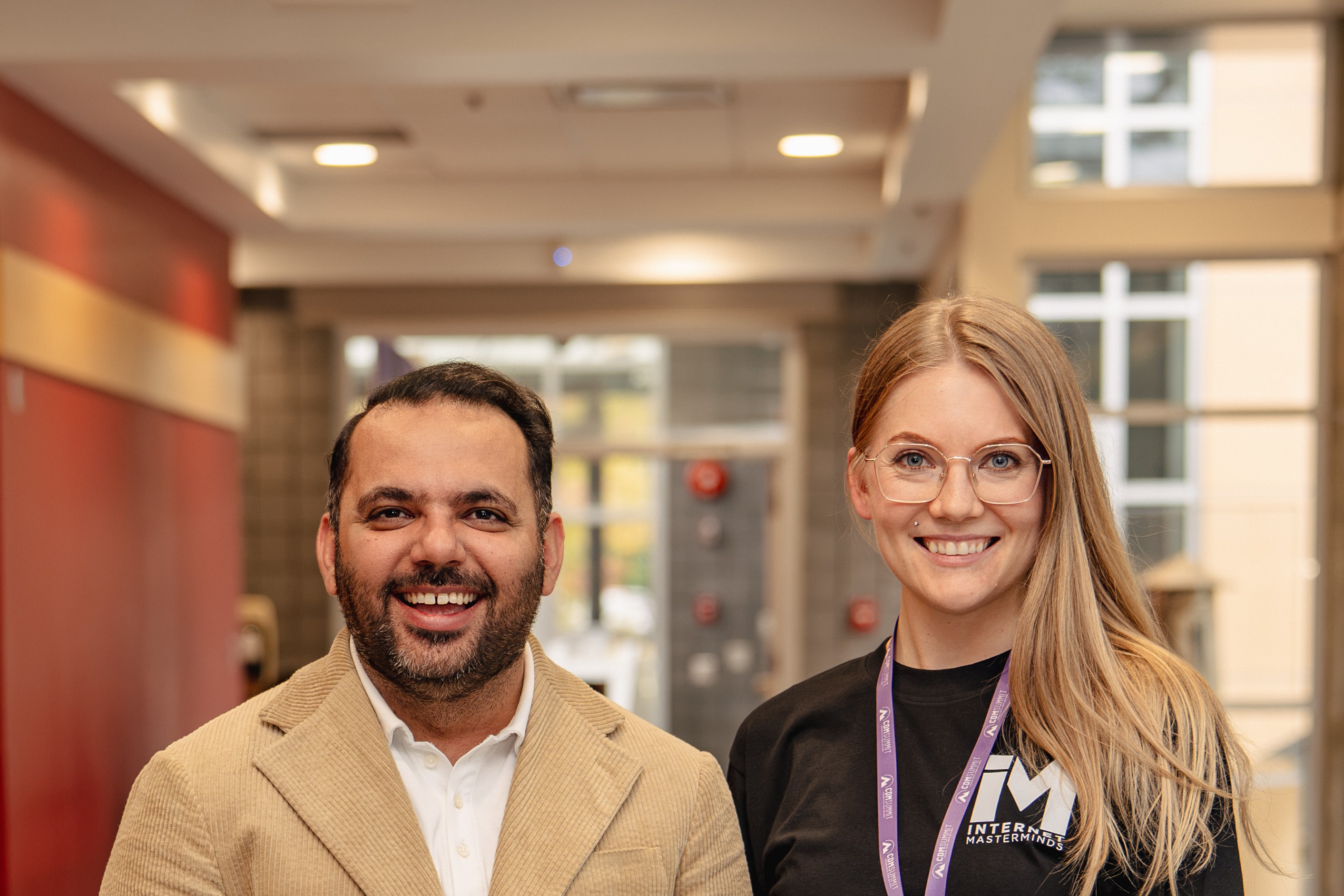 A smiling attendee in a tan blazer talking with a volunteer wearing a lanyard.