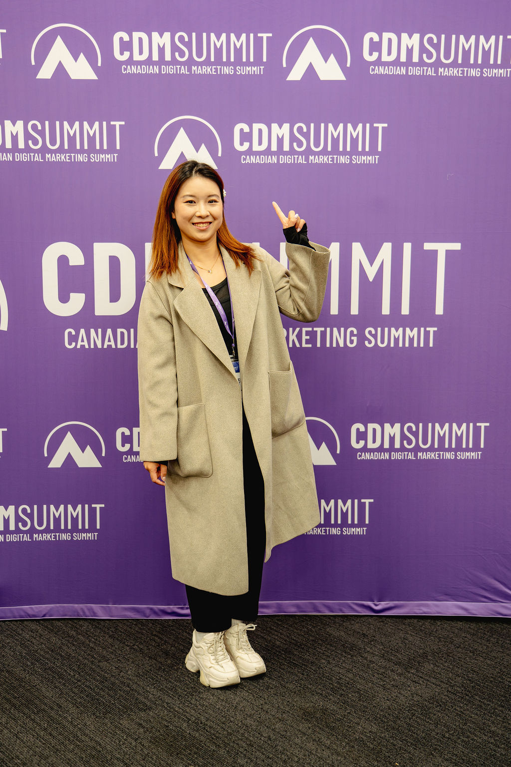 An attendee pointing at the purple CDM Summit backdrop